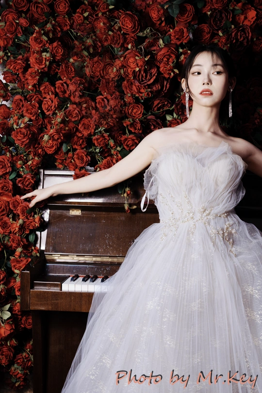 一位穿着白色连衣裙的美女在红玫瑰和钢琴前摆姿势