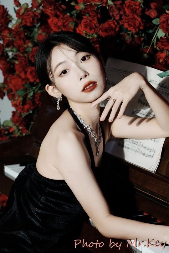 一位穿着黑色连衣裙的年轻女子在钢琴前摆姿势