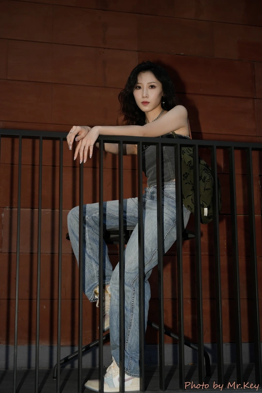 一位穿着牛仔裤和黑色上衣的年轻女子倚靠在栏杆上 倚靠在滑板车上 倚靠在黑色墙壁上