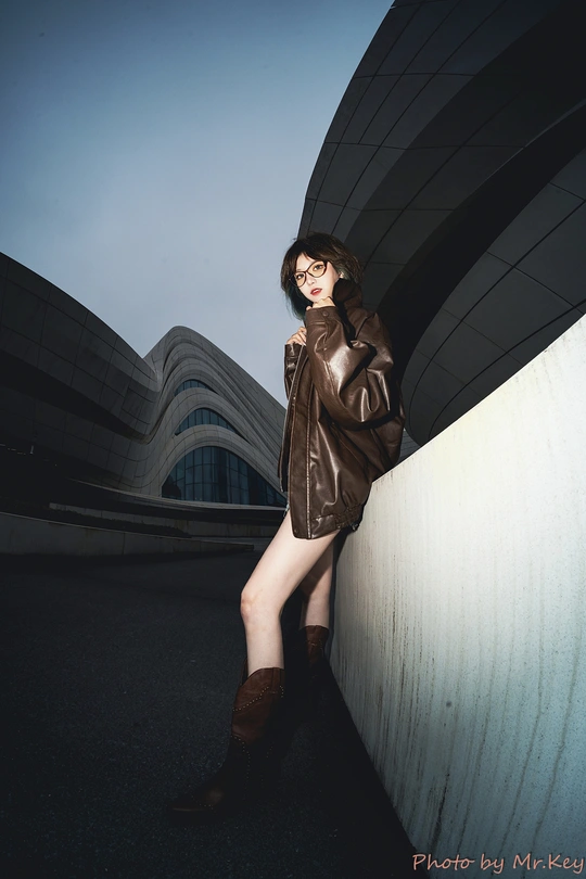 一位穿着棕色皮夹克和靴子靠在墙上的女人