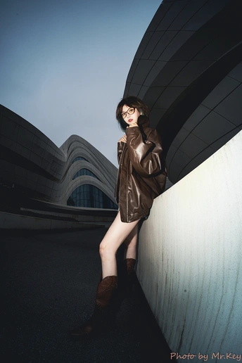 一位穿着棕色皮夹克和靴子靠在墙上的女人