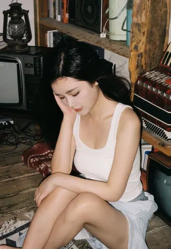 一个年轻女子坐在杂物堆满的房间里 前方有一台电视。