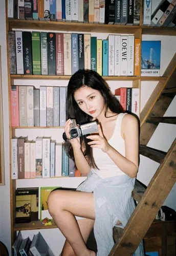 一位年轻女子坐在楼梯前 手里拿着相机 书架上堆满了书。