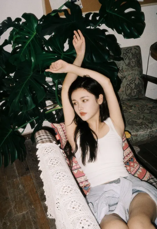 一个年轻女子坐在椅子上 双腿交叉在地面上 旁边有一盆植物。