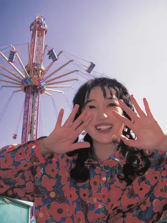 一个年轻女子面带微笑 双手举在过山车前的游乐园或嘉年华上。