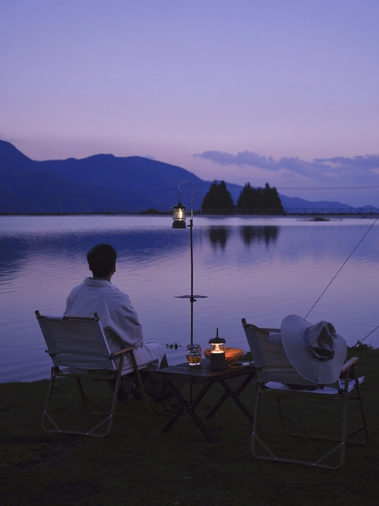一个人坐在椅子上 观赏着湖边的日落 同时有几个人在黄昏时分钓鱼。