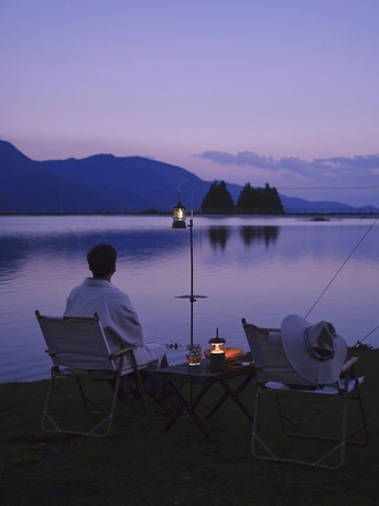 一个人坐在椅子上 观赏着湖边的日落 同时有几个人在黄昏时分钓鱼。