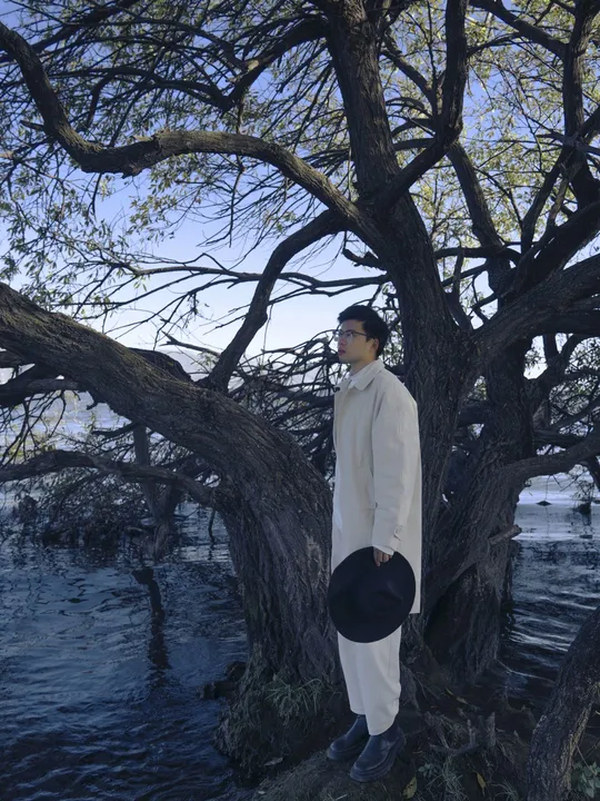 站在水边的一棵大树旁的戴帽男子