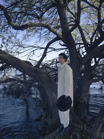站在水边的一棵大树旁的戴帽男子