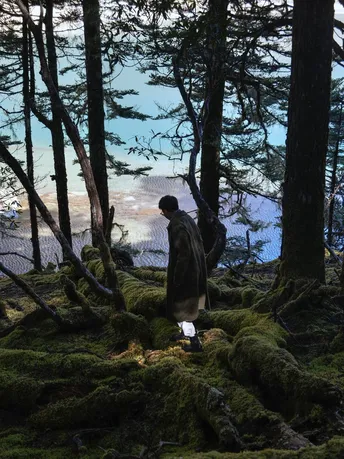 一个站在森林中的男人 周围长满了藓和树木 手里拿着灯笼。