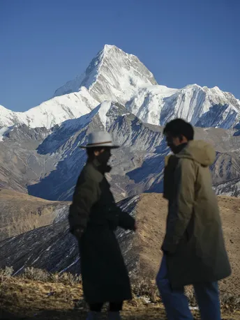 一个人和一个女人正在爬上一个有雪山背景的山坡。