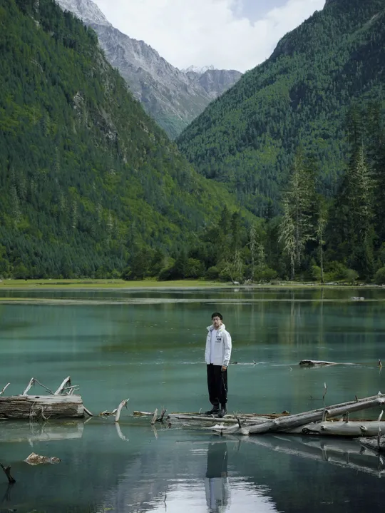 一位站在木头上的男人 周围环绕着山 湖泊环绕。