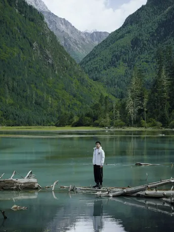 一位站在木头上的男人 周围环绕着山 湖泊环绕。