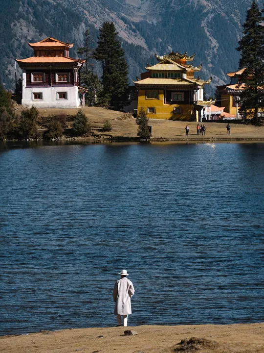 站在湖前的男子 背景有寺庙和山脉。