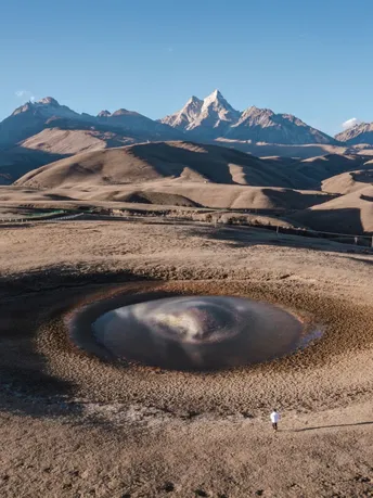 在一片沙漠中 一个人站在一个有湖泊的中间 背景是山脉。