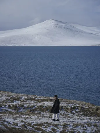 一个人站在一个雪覆盖的山坡上 眺望着一片水域。