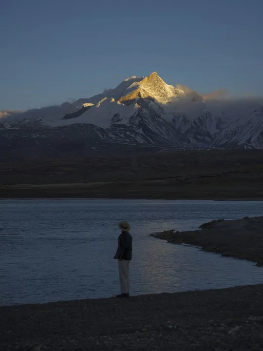 一个人站在河边 晚上看着一个被雪覆盖的山。