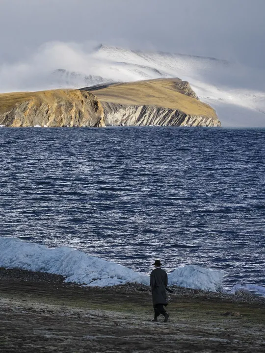 一个人在靠近水域的沙滩上行走 远处有山脉。