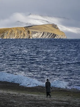 一个人在靠近水域的沙滩上行走 远处有山脉。