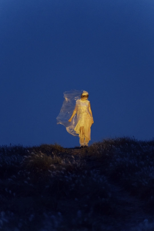 一位穿着白色连衣裙和黄色雨衣的女人在夜晚穿过田野 在月光下