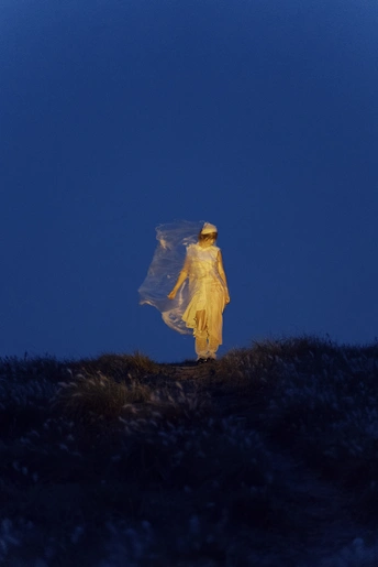 一位穿着白色连衣裙和黄色雨衣的女人在夜晚穿过田野 在月光下
