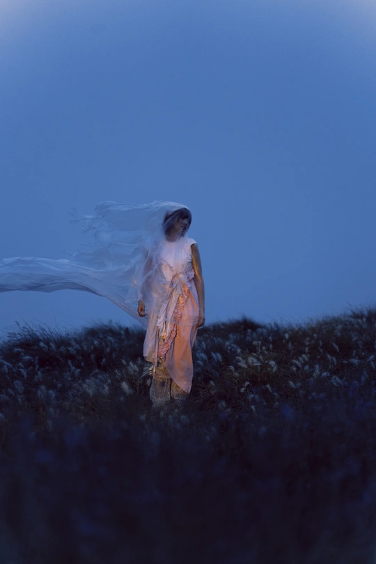 一个穿着白色连衣裙的女人在夜晚的田野中行走 周围有蓝色灯光。