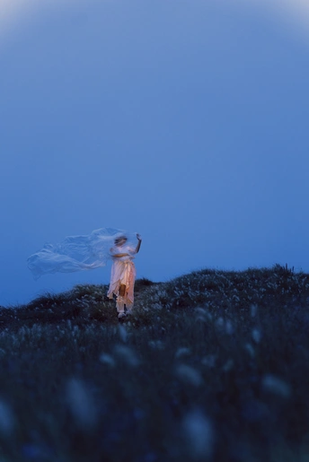 一个小女孩穿着蓝色裙子在夜晚沿着月光照耀的山坡走下去