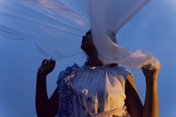 一位年轻女子穿着白色连衣裙和塑料面纱在风中对抗蔚蓝天空