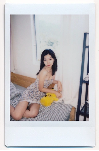 一个穿着连衣裙的年轻女子坐在床上抱着一个黄色毛绒玩具