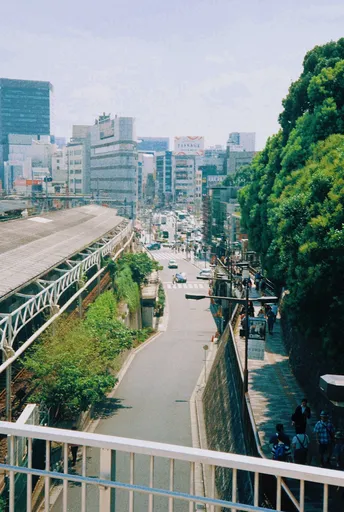 从桥上俯瞰一个城市中的火车站 有人们、树木、建筑和一条道路。