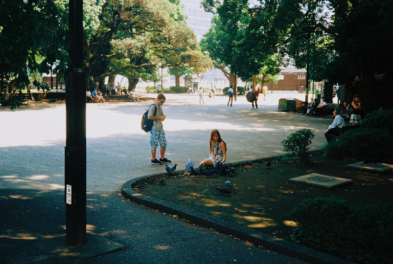 一个年轻女孩坐在滑板上 一个男子站在人行道上 背景中有人骑车。