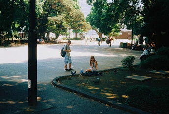 一个年轻女孩坐在滑板上 一个男子站在人行道上 背景中有人骑车。