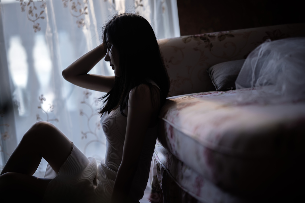 一个年轻的女人坐在有窗户的房间里的床上