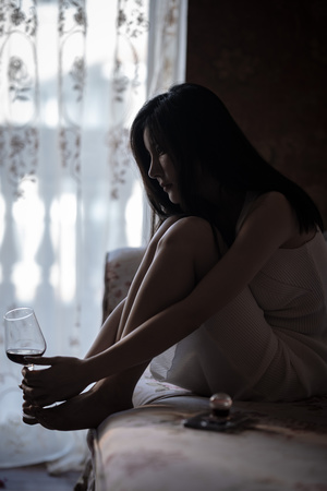 一个拿着一杯葡萄酒的年轻女子坐在窗前的床上