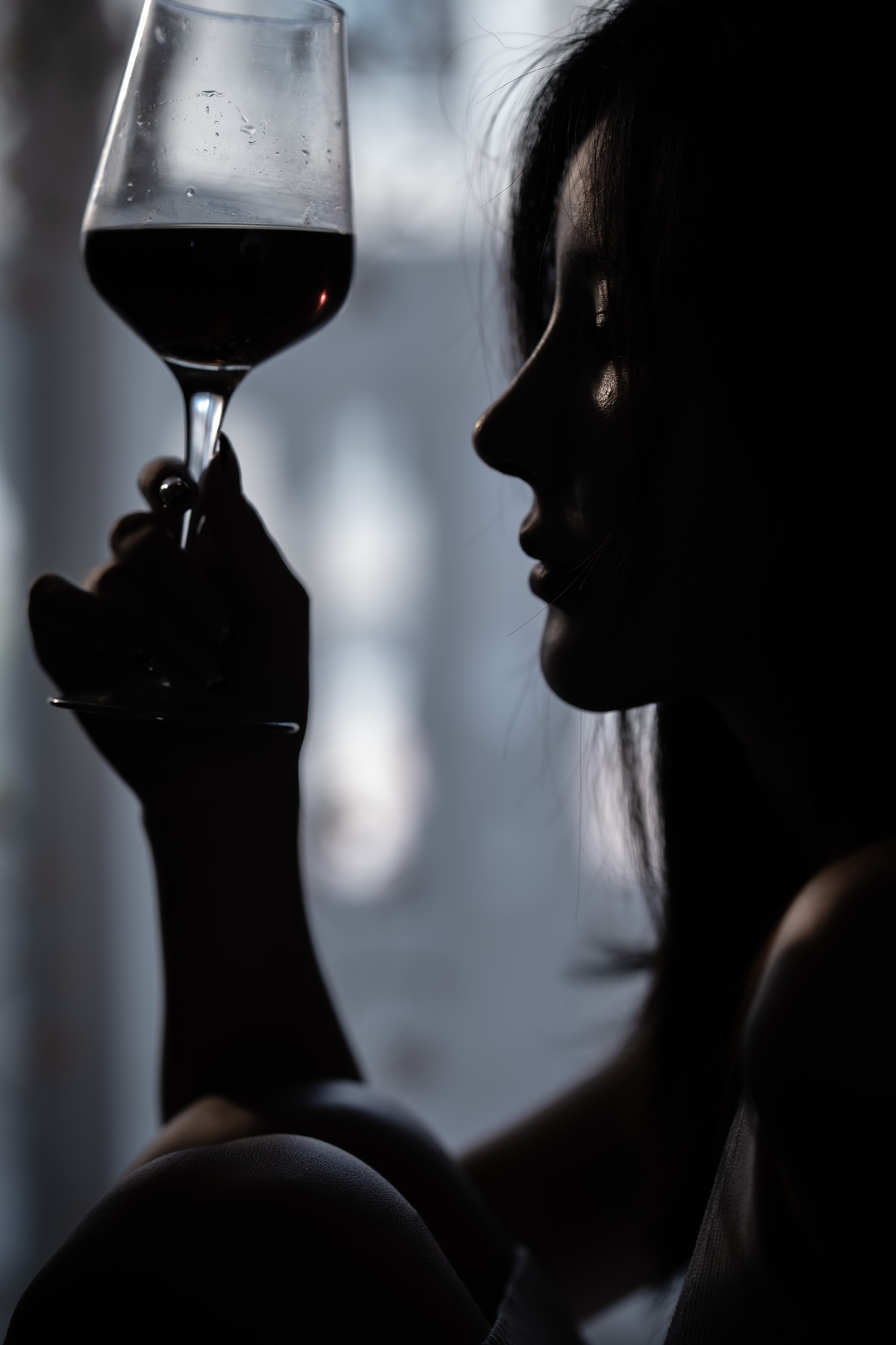 一个女人在窗前拿着一杯红酒的剪影