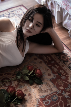 一个穿着白色连衣裙的年轻女子躺在卧室的地板上 卧室里铺着地毯 床上放着红玫瑰