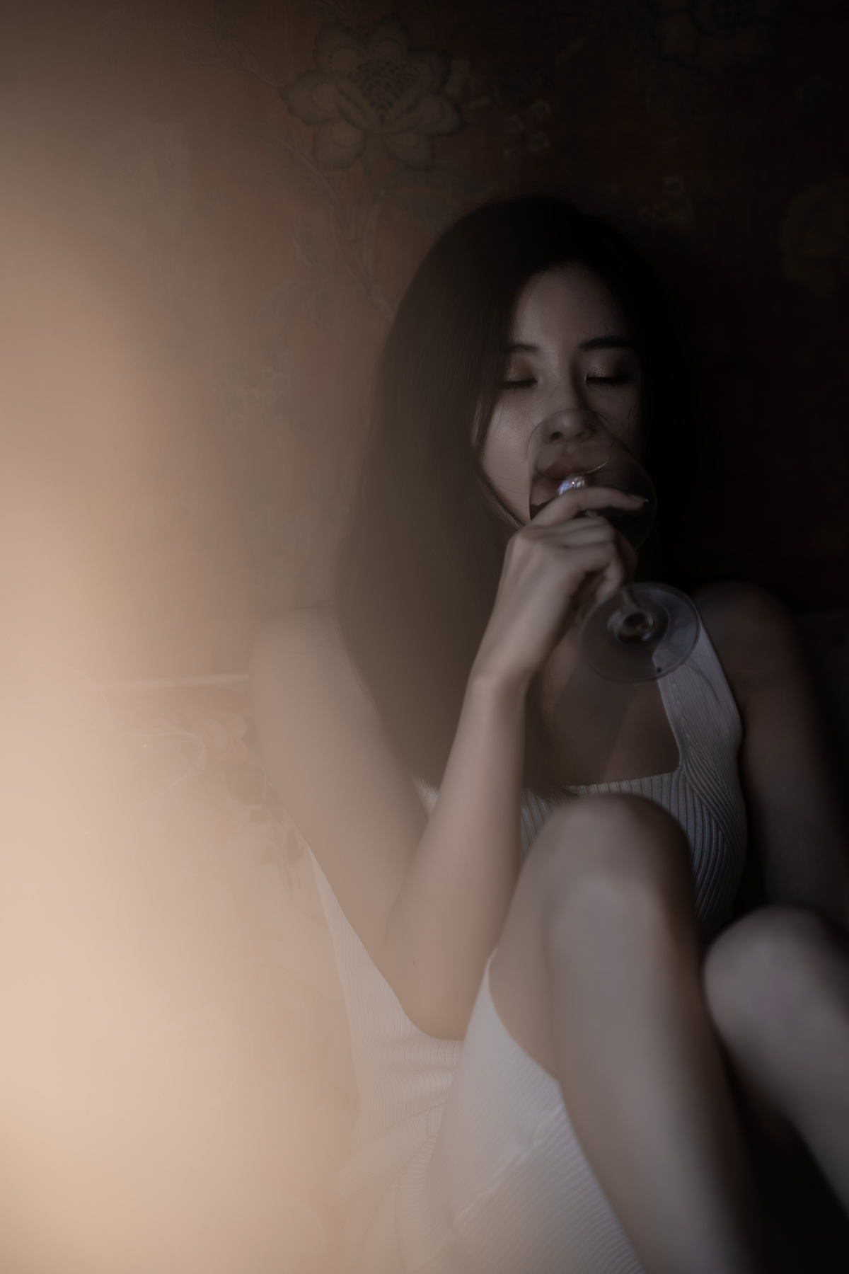 一个年轻女人坐在黑暗的房间里的床上抽烟喝酒
