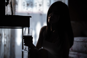 一个黑暗的房间里 一个年轻女人手里拿着一杯葡萄酒的黑色剪影