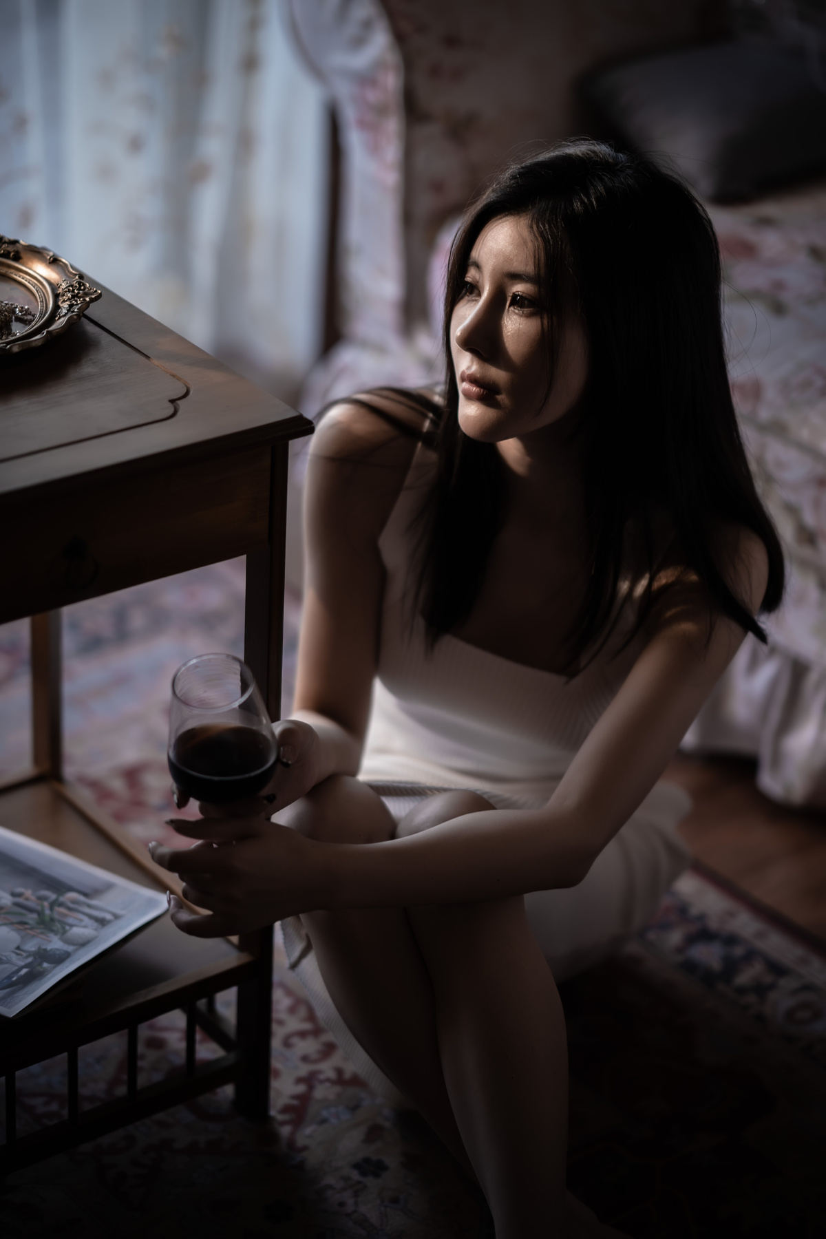 一个手里拿着一杯红酒的年轻女子坐在一个有床和桌子的房间里