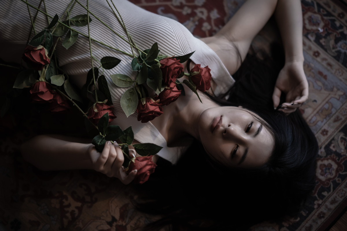 一个年轻的女人拿着红玫瑰躺在地板上 摆出一个死去的女人的姿势