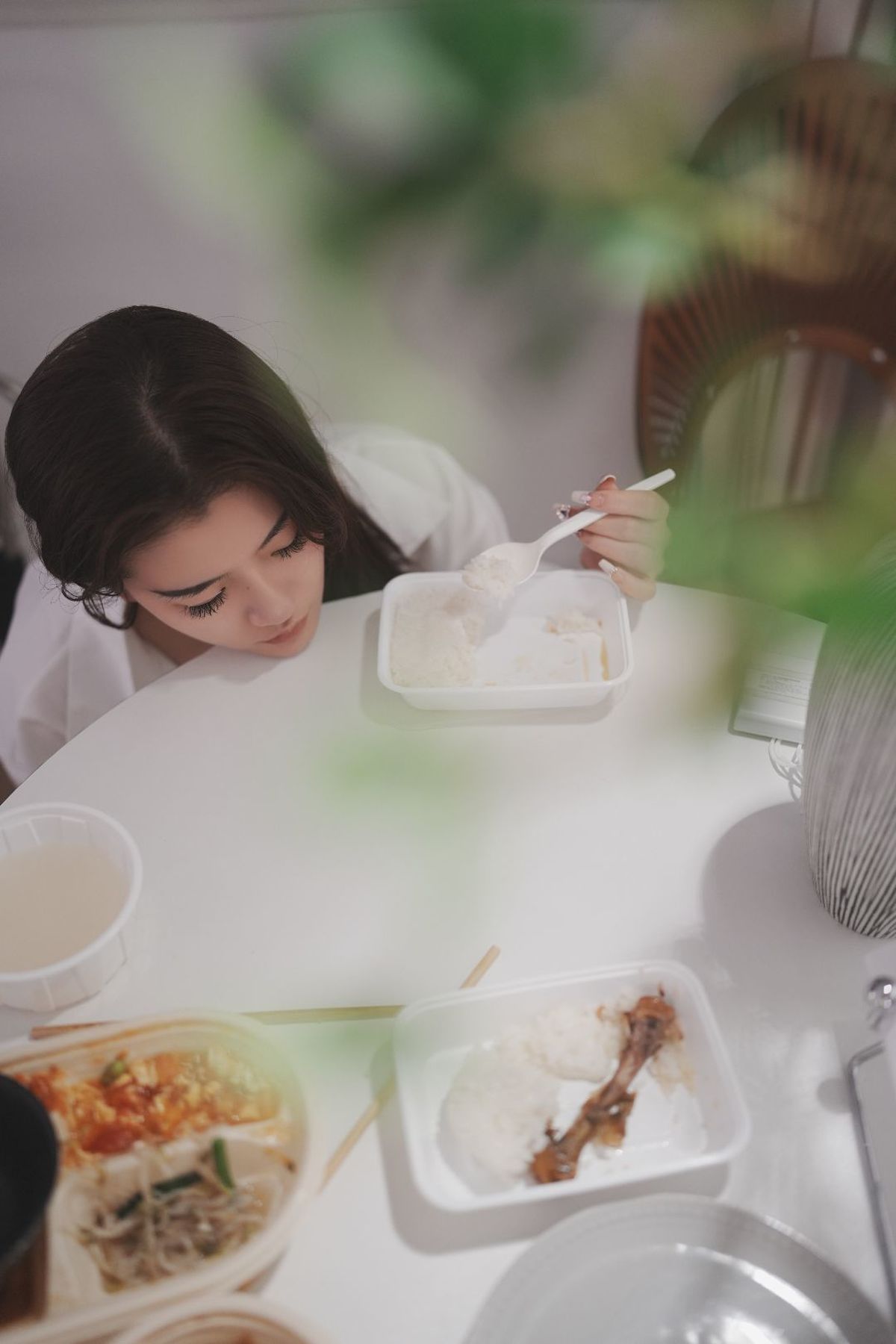 一位年轻女子坐在桌子旁 吃着从白盘子里的饭。