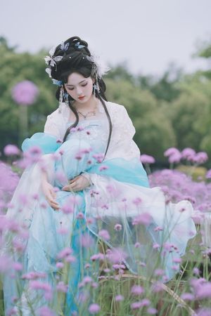 一位穿着传统蓝色连衣裙的美丽年轻女士 置身于紫花丛中。