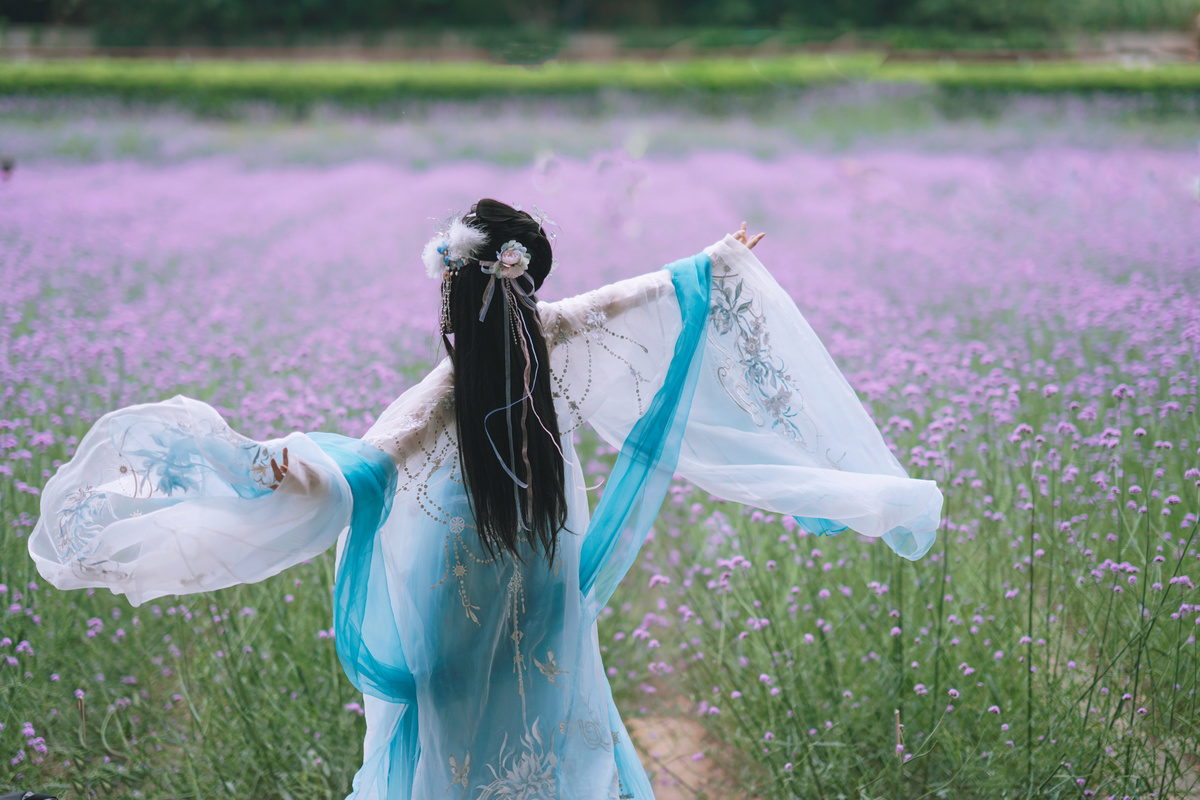 一位穿着传统裙子的美丽年轻女子 穿过薰衣草花田 头发中夹杂着紫色的花朵。