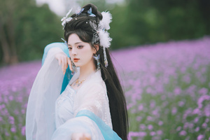 一位美丽的年轻女子 蓝发 身着传统服装 置身于薰衣草花田中 花田中还点缀着紫色的花朵。
