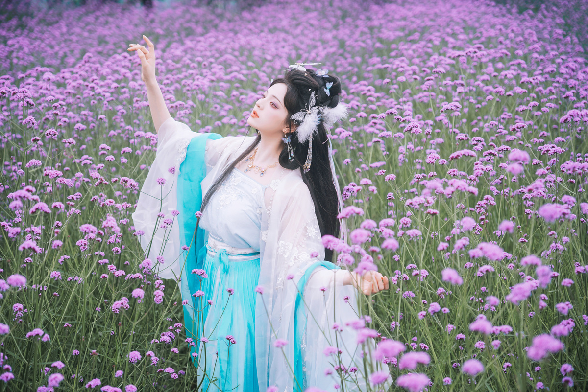 一位穿着蓝色连衣裙的美女站在紫花丛中