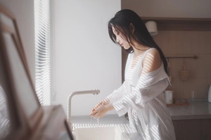 一个年轻女子在白色的厨房里洗着手 同时看着水槽里的水龙头。