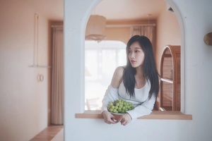 一张年轻女子拿着一个装满绿葡萄的碗 正在透过窗户向外看