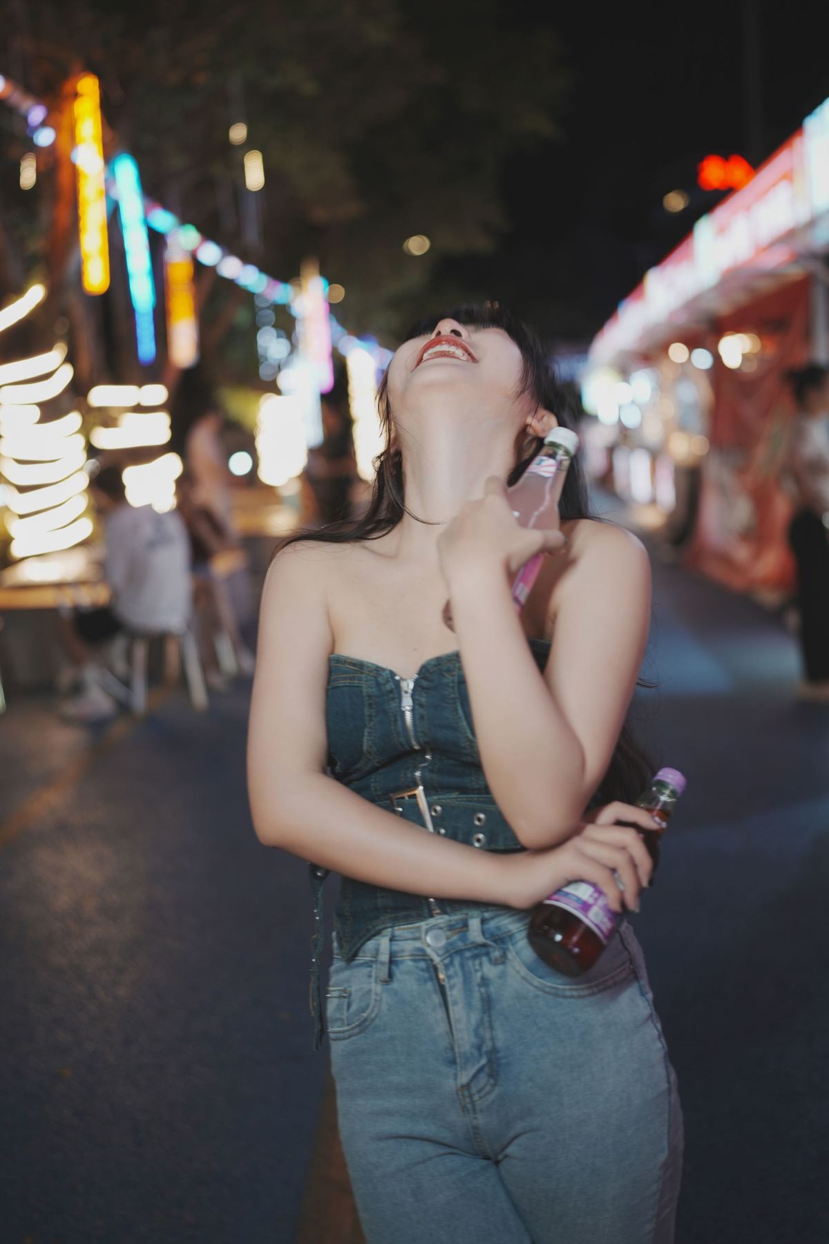 一个年轻女子口含饮料 正在通话中 站在夜晚的街头中央。