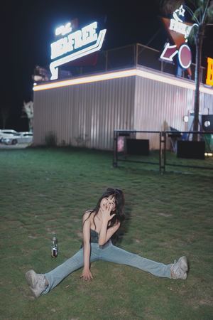 一个年轻女子穿着牛仔裤坐在汽车旅馆的草坪上 另一个女孩躺在草地上。