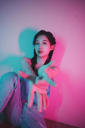 一位年轻女子坐在粉红色墙壁和蓝色灯光的房间里的肖像